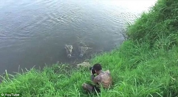 鲁伊斯蹲坐在河边,手里拿着相机拍摄河中的鳄鱼