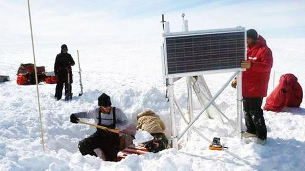 研究人员围绕着一个地震仪辛苦的工作着,装在橙色盒子中的地震仪将被埋入到一个雪洞中。