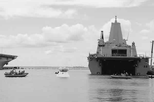 漂浮在海上的白色舱体为“猎户座”飞船模拟载人舱,海军正牵引着载人舱向“阿灵顿”号两栖船坞运输舰方向移动。