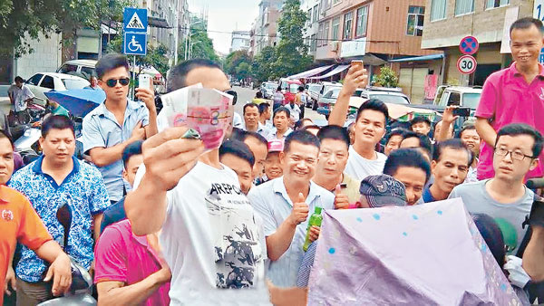 狗贩挥舞钞票炫耀引围观民众起哄,更有人竖起拇指。