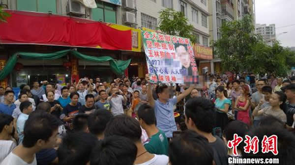 一名有自我炒作嫌疑者在狗肉餐馆前举牌“抗议”,被围观者嘲笑,最终遭政府人员带离现场。