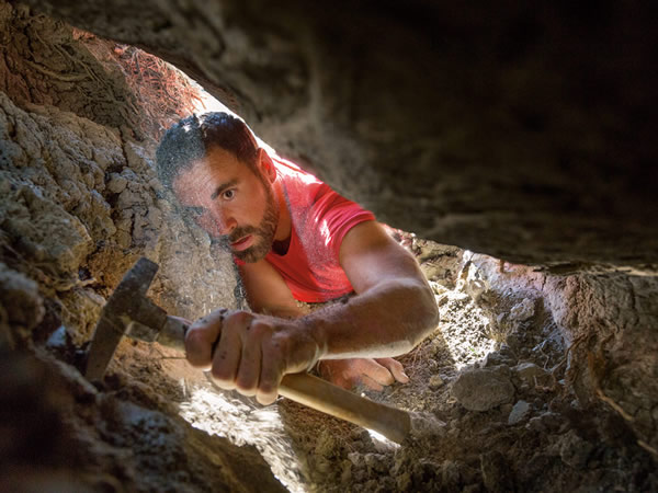 在犹他州南部一处沙漠探勘化石的古生物学家乔.瑟尔提克刮去一颗巨砾下的泥土,他在那里发现了一只年轻恐龙的皮肤与骨骼碎片。 PHOTOGRAPH BY CORY R