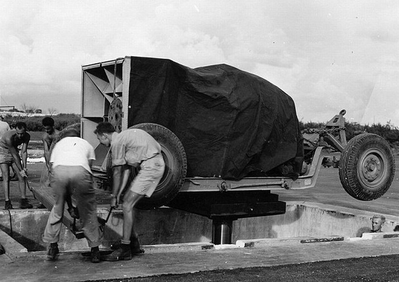 工作人员使用液压起重机和金属槽将原子弹放进大坑中,并用布遮住